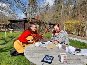 Dos obreras en un ambiente agradable, al aire libre, con una guitarra, cantando, y con libros en una mesa al lado.